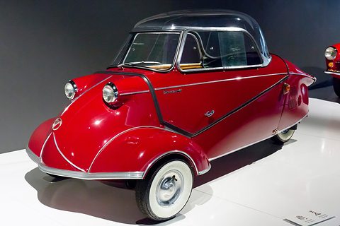 Red bubble car with dark-tinted canopy and whitewall tyres on a white plinth. Opens a larger view