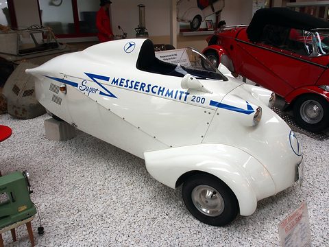 Long white streamlined body with a headrest fairing and blue lettering, side-on on gravel. Opens a larger view