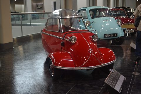 Red bubble car head-on on a dark floor, a turquoise Isetta behind. Opens a larger view