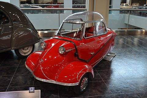 Red bubble car with clear canopy on a dark polished floor, a grey Citroën beside it. Opens a larger view