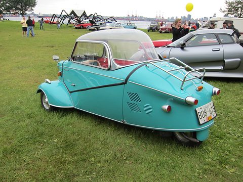 Turquoise tapering tail with chrome rack on grass, a waterfront and visitors behind. Opens a larger view