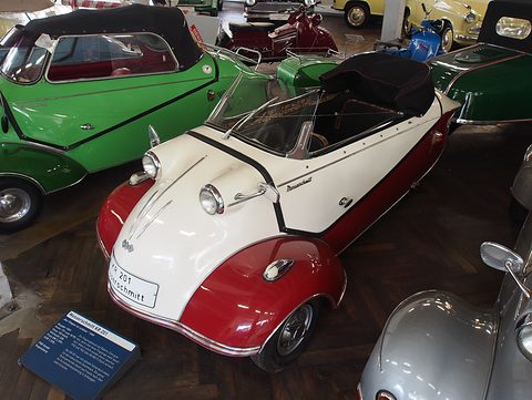 White over red open microcar with folded black hood on a parquet museum floor. Opens a larger view