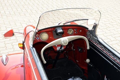 Cream handlebar steering in front of a red dashboard with round instruments, behind a clear screen. Opens a larger view