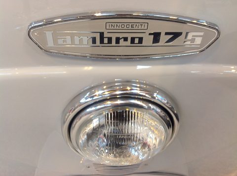 Close view of a chrome Lambro 175 badge above a round chrome headlamp on grey paint. Opens a larger view