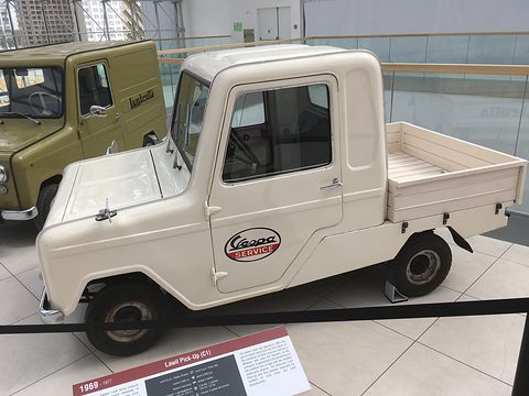 Cream microcar pick-up with a short cab, a wooden-sided load bed and a red oval Vespa Service decal on its door. Opens a larger view