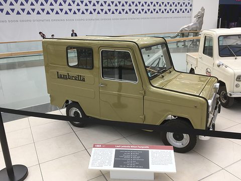 Olive green boxy microcar van with Lambretta script on its side, behind a rope with an information board in front.
