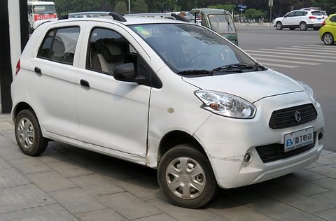 White small four-door hatchback with large headlamps and a chrome-trimmed grille parked on paving.