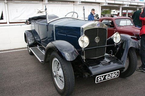 Dark blue open tourer with a tall black radiator, wire wheels and a white number plate. Opens a larger view