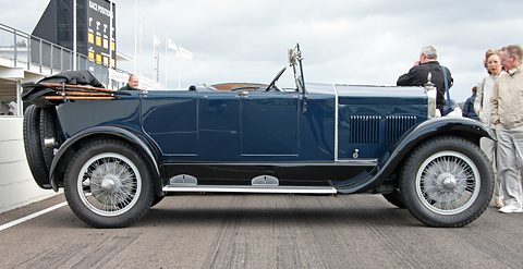 Side view of a long dark blue open tourer with wire wheels, people talking beside it. Opens a larger view