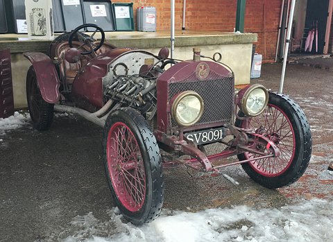 Maroon open special with an exposed engine, wire wheels and big lamps on a snowy yard. Opens a larger view
