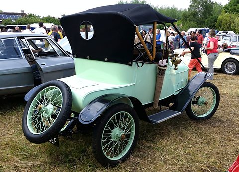 Pale green two-seater with wire wheels, a spare on the side and a black hood, on grass. Opens a larger view
