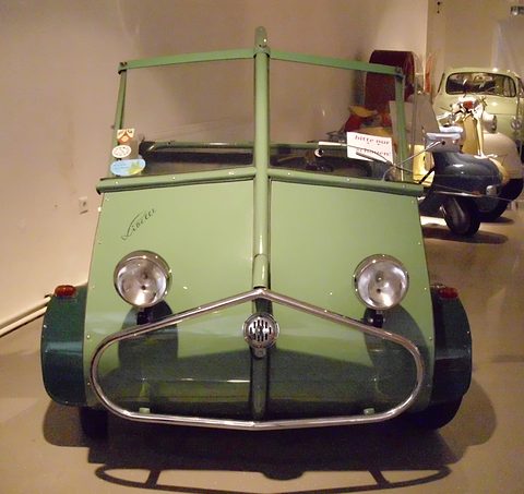 Green open three-wheeler with a chrome bumper bar and tubular hood frame, two headlamps. Opens a larger view