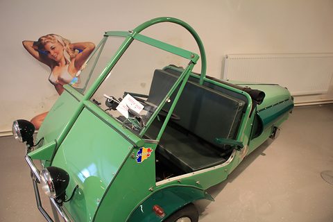 Green open three-wheeler with a curved hood frame, seen from above at the front quarter. Opens a larger view