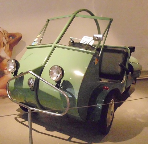 Green open three-wheeler with a hood frame and chrome nose bar, a pin-up cut-out behind.