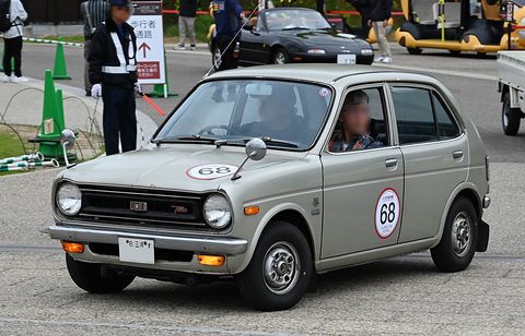 Silver-grey small four-door saloon with rally number 68 on its doors and bonnet, driving past a marshal on tarmac. Opens a larger view