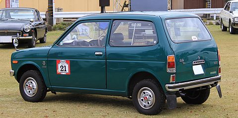 Rear quarter of a dark green small three-door van with a number 21 on its door, on a lawn with classic cars behind. Opens a larger view