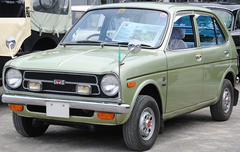 Pale green small four-door saloon with round headlamps, auxiliary lamps and a chrome grille, a notice on the dashboard. Opens a larger view