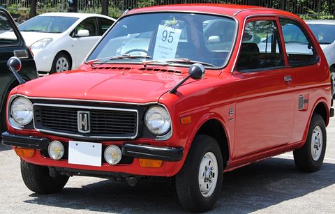 Red small four-door saloon with round headlamps, a black grille with the H badge and fog lamps, a show number on the windscreen. Opens a larger view