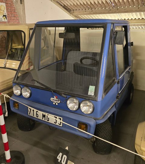 Pale blue boxy two-seater with four small round headlamps and French plate 716 MG 33, a rope barrier across it.