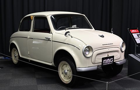 Cream rounded small saloon with a gallery number plate, against black drapes on a grey carpet. Opens a larger view