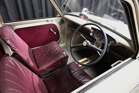 Through an open door: maroon front seats, a large black steering wheel and a cream metal dashboard. Opens a larger view