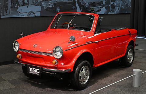 Red open two-door small car with round headlamps and a gallery plate, on a dark carpet. Opens a larger view