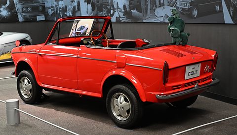 Rear three-quarter of a red open car with a Colt badge on the tail and a small figure on the rear deck. Opens a larger view