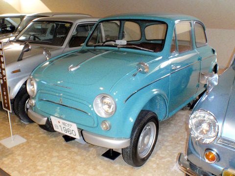 Turquoise rounded small saloon on a beige floor among other old cars in a museum. Opens a larger view