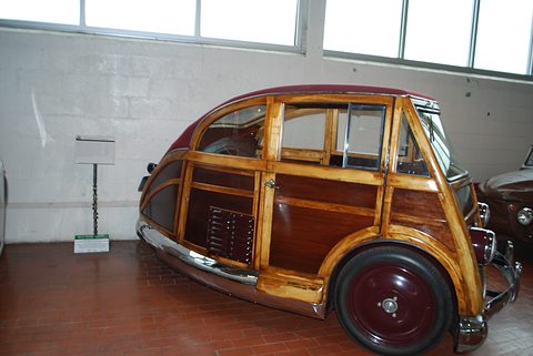 Small varnished wooden estate car with maroon wheels, chrome bumpers and a maroon roof, on a brick museum floor.