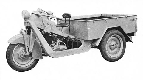 Pale grey three-wheeled truck in a black and white studio view, step-through frame, saddle and long cargo bed. Opens a larger view