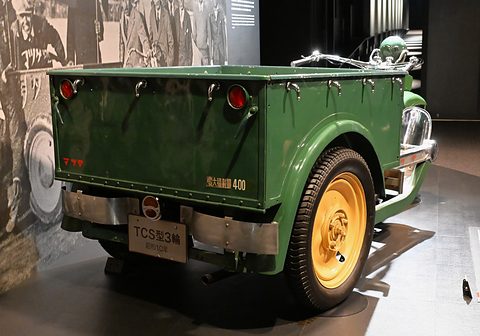 Rear of a green three-wheeler: steel cargo box with a 400 kg marking, a plate reading TCS and twin rear wheels. Opens a larger view
