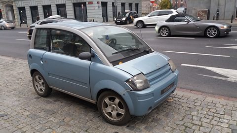 Pale blue small hatchback on a cobbled pavement, cars on the road behind. Opens a larger view