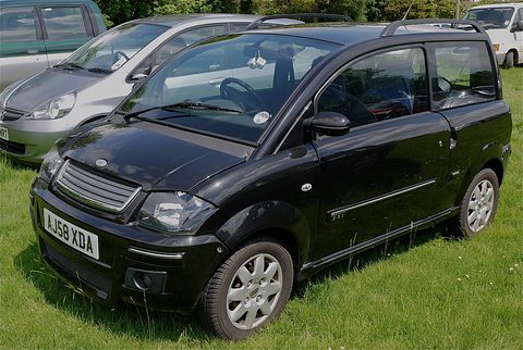 Black small hatchback with a slatted grille and alloy-look wheels parked on a lawn.