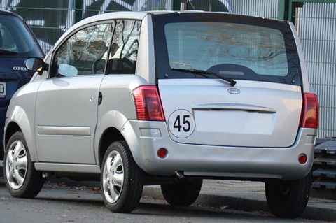 Rear of a silver microcar with tall tail lamps and a round 45 speed disc, plate blanked.