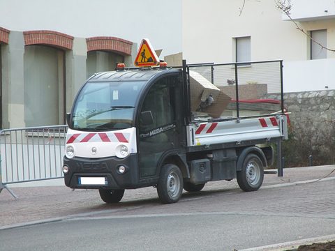 Black and white small electric utility truck with a cage body and an orange triangle on its roof on a street. Opens a larger view
