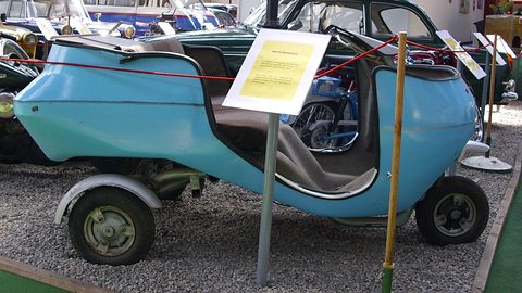 Long pale blue open body with two front wheels and an information placard on a pole beside it. Opens a larger view