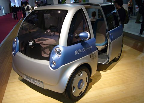 Silver and blue tall microvan concept with a sliding door open on a wooden show floor. Opens a larger view