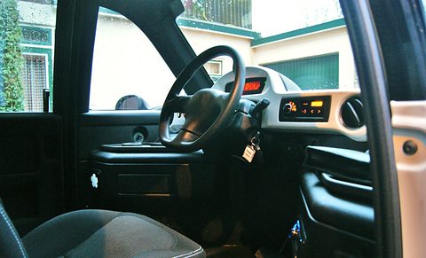 Single central driver’s seat behind a steering wheel and slim dashboard, seen through the open side door.
