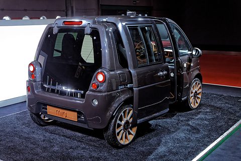 Dark grey tall microvan with copper-coloured wheels and open tailgate on a shaggy blue carpet. Opens a larger view