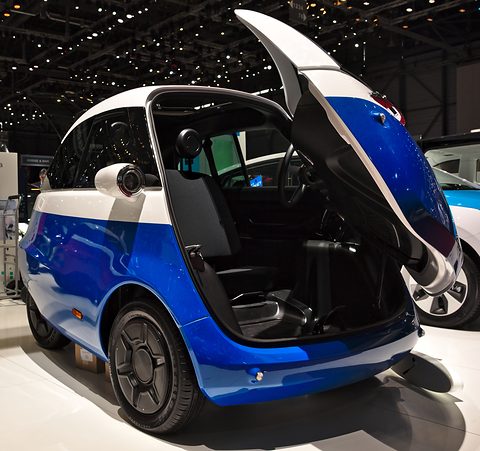 Blue and white bubble car with its front swung up, showing the steering column and a bench seat inside. Opens a larger view