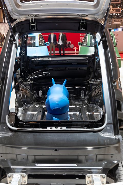 Rear of an unpainted car body with the tailgate open, showing the load floor with a blue toy animal on it. Opens a larger view
