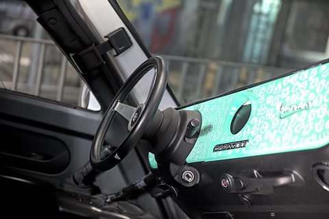 Black three-spoke steering wheel and a turquoise dashboard panel with white doodles and a row of switches. Opens a larger view