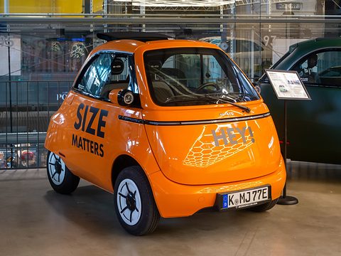 Orange bubble car with large SIZE MATTERS lettering on its side, parked on a hall floor beside an information stand. Opens a larger view