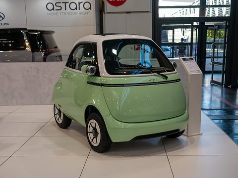 Pale-green and white bubble car with chrome lamp pods on a tiled floor beside a dealer counter. Opens a larger view