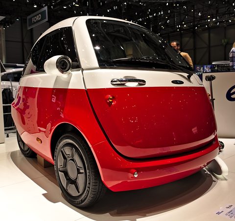 Red and white bubble car with chrome handle and round lamp pods on a white show floor. Opens a larger view