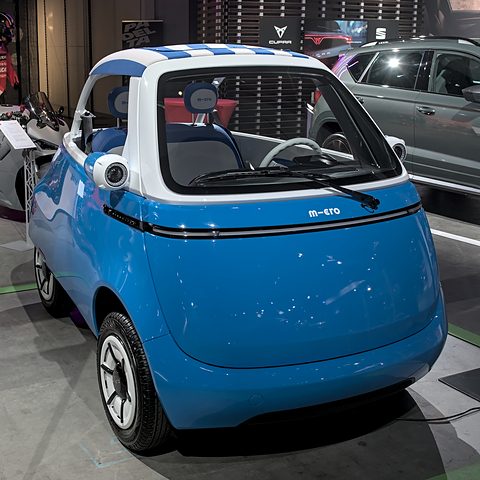Open blue bubble car with a blue and white striped canopy and no doors, on a show floor. Opens a larger view