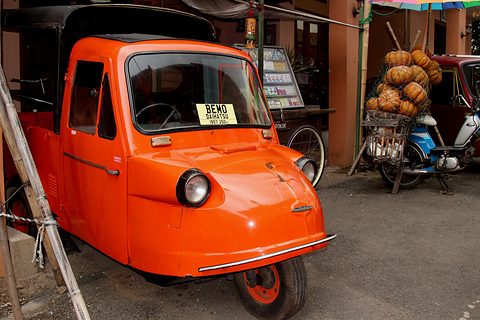 Bright orange three-wheeled vehicle with a closed passenger body and a BEMO sign in its windscreen. Opens a larger view