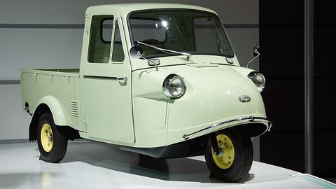 Pale green three-wheeled pickup with a closed cab, round headlamps on a curved nose and yellow wheels. Opens a larger view