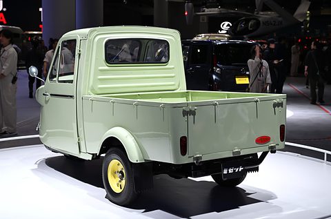 Rear three-quarter of a pale green three-wheeled pickup with a drop-down tailgate on a white turntable. Opens a larger view