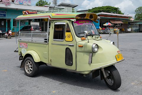 Pale green three-wheeled taxi with a colourful roof rack and canopy, round headlamps and a yellow plate.